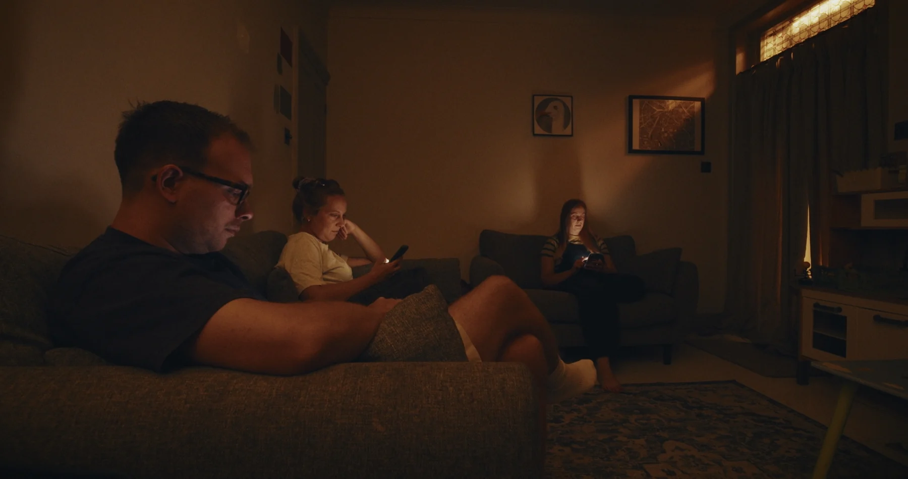 A family sitting together while looking at their phones in a dim room
