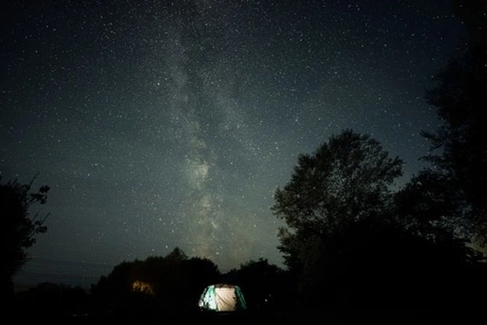 The Milky Way above a dark campsite with a softly lit tent below