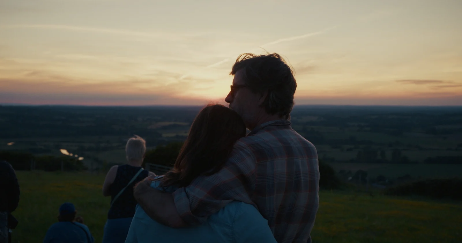 Two people holding one another while watching the sunset from a hill
